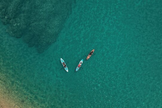 Aerial view showcasing friends kayaking in crystal-clear turquoise sea on a sunny summer day