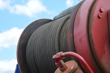 A close-up of a large industrial winch drum, tightly spooled with thick steel wire rope, against a...