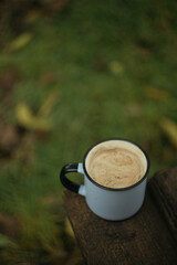 Cup of coffee with milk on a wooden stump in the forest
