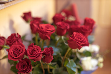 A vibrant bouquet of fresh red roses stands prominently, with some white blooms subtly visible in the soft background.