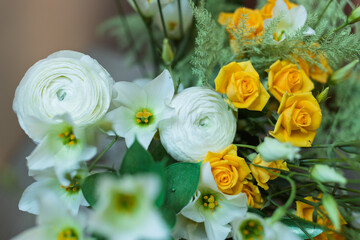A vibrant close-up captures a fresh bouquet featuring delicate white ranunculus, star-shaped white flowers, and bright yellow roses with lush green foliage.