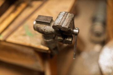 A sturdy, old metal bench vise is clamped securely to a wooden workbench in a workshop setting, ready for use.