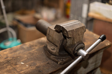 An old, well-used metal workbench vise is securely mounted on a rustic wooden table in a workshop setting.