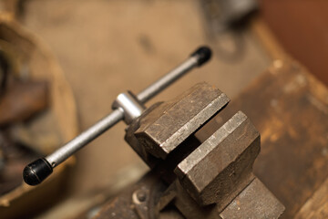 A close-up shot of an old, rusty metal vise on a blurred workbench, ready to hold objects securely.