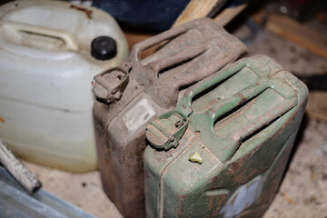 Three weathered fuel containers, including a white plastic jug and two rusty metal jerry cans, are...