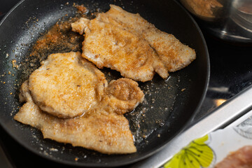 Golden brown breaded cutlets sizzle in a hot frying pan on a stovetop, ready to be flipped.
