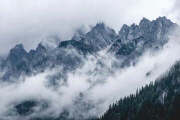 Jagged mountain range peaks obscured by low-hanging, swirling clouds, lush forest below