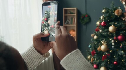 Close up on phone screen in hands of Black woman recording video of little daughter and husband topping Christmas tree with star ornament in decorated living room, family creating happy memories