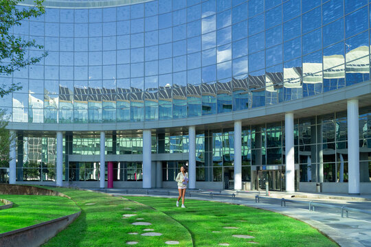 Young woman walking on a green lawn with a contemporary glass office building in the background