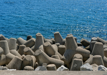Obraz premium Close-up view of interlocking concrete tetrapods forming a breakwater against the sparkling blue sea.