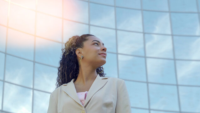 Young businesswoman looking up with a visionary expression in front of a modern glass building