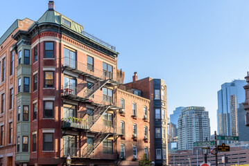 Traditional brick apartment building with metal balconies and escape stairs in Boston at sunset in autumn. Modern high rise office buildings are visible in background.