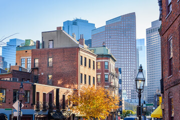 Traditional brick residential buildings overlooked by towering modern office skyscrapers in Boston at sunset in autumn