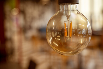 A classic designed tungsten lightbulb is glowing in orange warmlight shade with blurred background 