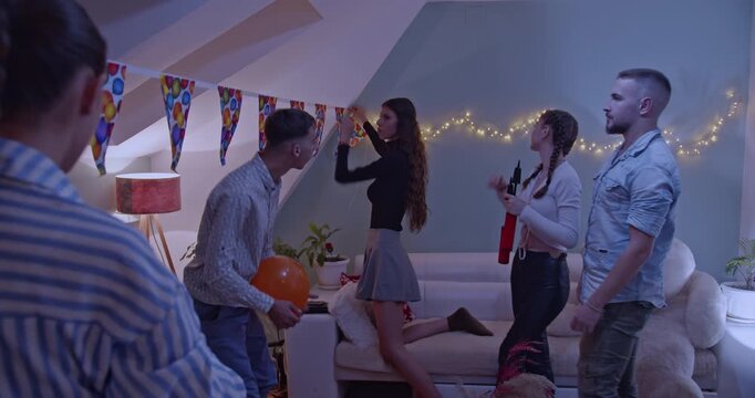 A group of excited young friends are joyfully decorating their home, hanging colorful party banners and string lights, preparing for a festive birthday party celebration filled with fun and laughter.