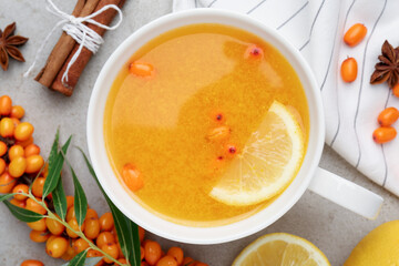 Sea buckthorn tea in cup, spices, lemon and fresh berries on light grey table, flat lay