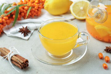Sea buckthorn tea in glass cup, teapot, spices, lemon and fresh berries on light grey table, closeup