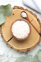 Sea salt in bowl, spoon, towels and eucalyptus leaves on white marble table, flat lay
