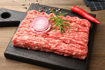 Raw minced meat with rosemary, thyme and spices on wooden table, closeup