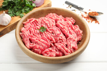 Raw minced meat, parsley and spices on white wooden table, closeup