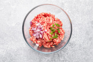 Raw minced meat with onion and parsley in bowl on grey table, top view