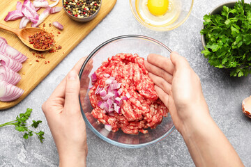 Woman stirring raw minced meat with onion in bowl at grey table, top view