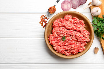 Raw minced meat, parsley, spices and onion on white wooden table, flat lay. Space for text