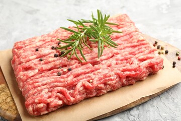 Raw minced meat with peppercorns and rosemary on grey textured table, closeup