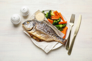 Salt, pepper shakers, tasty roasted dorado fish, vegetables, sauce and cutlery on light wooden table, flat lay