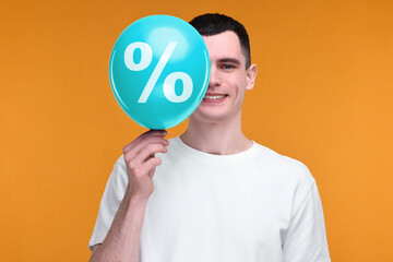 Man holding cyan balloon with percent sign on orange background. Discount offer