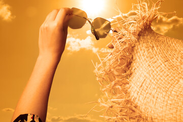 Woman holding sunglasses against orange sky with bright sun, closeup