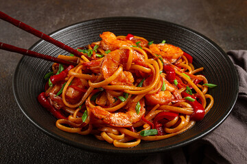 udon stir-fry shrimp noodles with red bell pepper and green onion, served in a black bowl, with chopsticks, dark background,