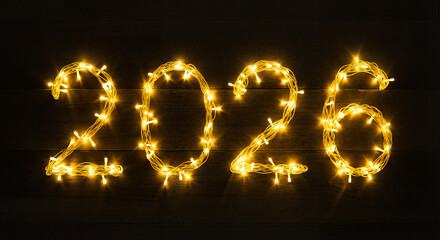Glowing 2026 numbers made of yellow Christmas lights on dark wooden background