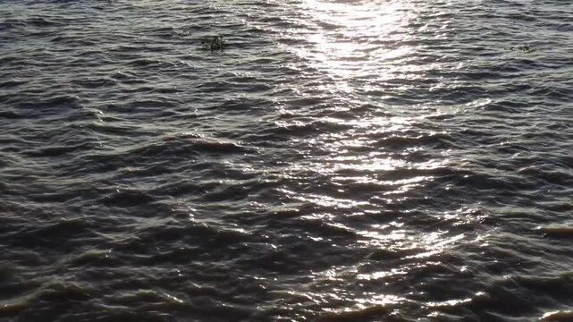Golden reflection of sunlight on the waves of a river as seen from a moving ship at sunset.