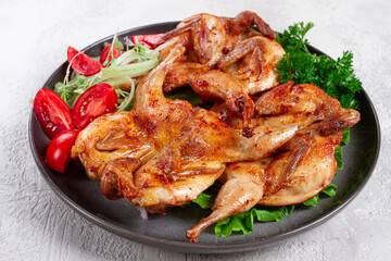 Baked quail, served on a plate with crispy lettuce leaves, fresh tomatoes and herbs, on a dark plate, homemade,