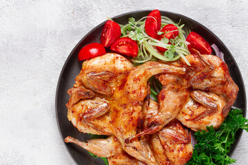 Baked quail, served on a plate with crispy lettuce leaves, fresh tomatoes and herbs, on a dark plate, homemade,