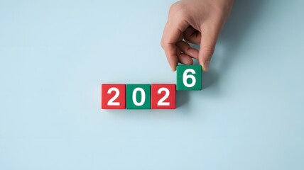 Hand placing a green block with the number six on top of red and green blocks spelling out the year 2026