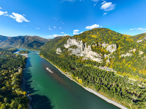 Panoramic aerial view of the wide, emerald Katun River flowing past a dense forest and a dramatic white limestone cliff face on a sunny day - Powered by Adobe