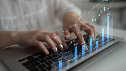 A focused individual types on a laptop while financial graphs and data trends overlay the image....