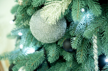 Close-up of a Large Silver Glitter Christmas Ornament on a Green Pine Branch with LED Lights