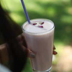 A person is holding a glass of pink liquid with a straw in it