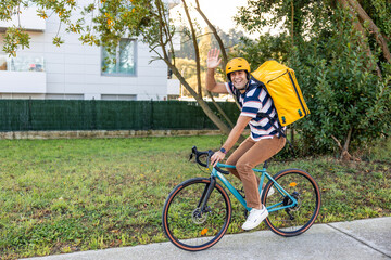 Naklejka premium Hispanic delivery man cycling, waving hand, smiling
