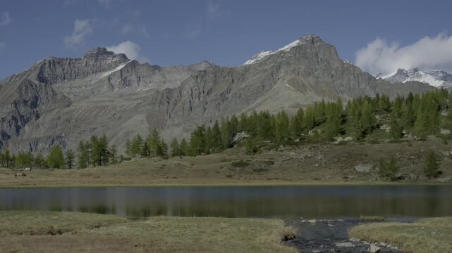 ideo of Dres Lake, Ceresole Reale, in Gran Paradiso National Park, Italy. Quick cloud shadows drift over turquoise alpine waters and peaks under a bright sunny sky in the Italian Alps.