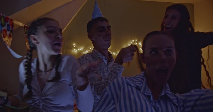 A group of excited young friends gathered at home, joyfully celebrating a birthday party. They are dancing, singing, and having an unforgettable night filled with laughter and good vibes.