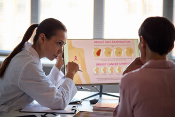 Caucasian female doctor explaining breast cancer symptoms to middle aged Caucasian woman using...