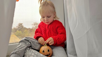 A little girl holds a pumpkin on Halloween, preparing for the celebration