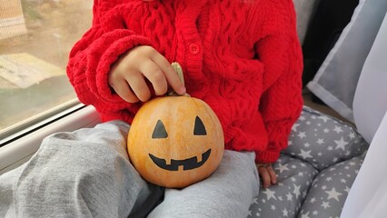 A little girl holds a pumpkin on Halloween, preparing for the celebration