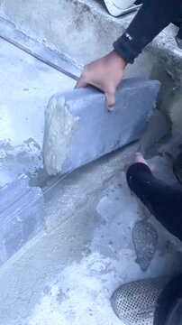 Construction worker laying concrete blocks with cement mortar at building site. Close-up of hands during masonry work under sunlight, showing texture and building process.