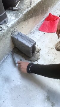Construction worker laying concrete blocks with cement mortar at building site. Close-up of hands during masonry work under sunlight, showing texture and building process.
