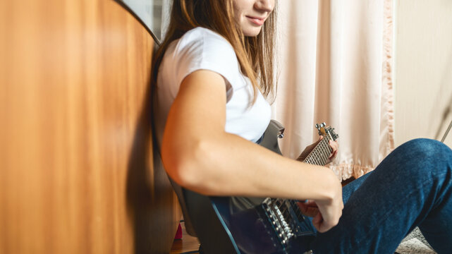 Young caucasian brunette woman sitting on floor and playing electric guitar at home - Powered by Adobe